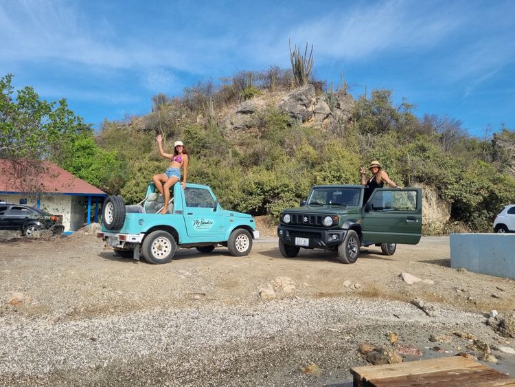 Two people pose with blue and green off-road vehicles on a rocky, arid landscape under a blue sky.